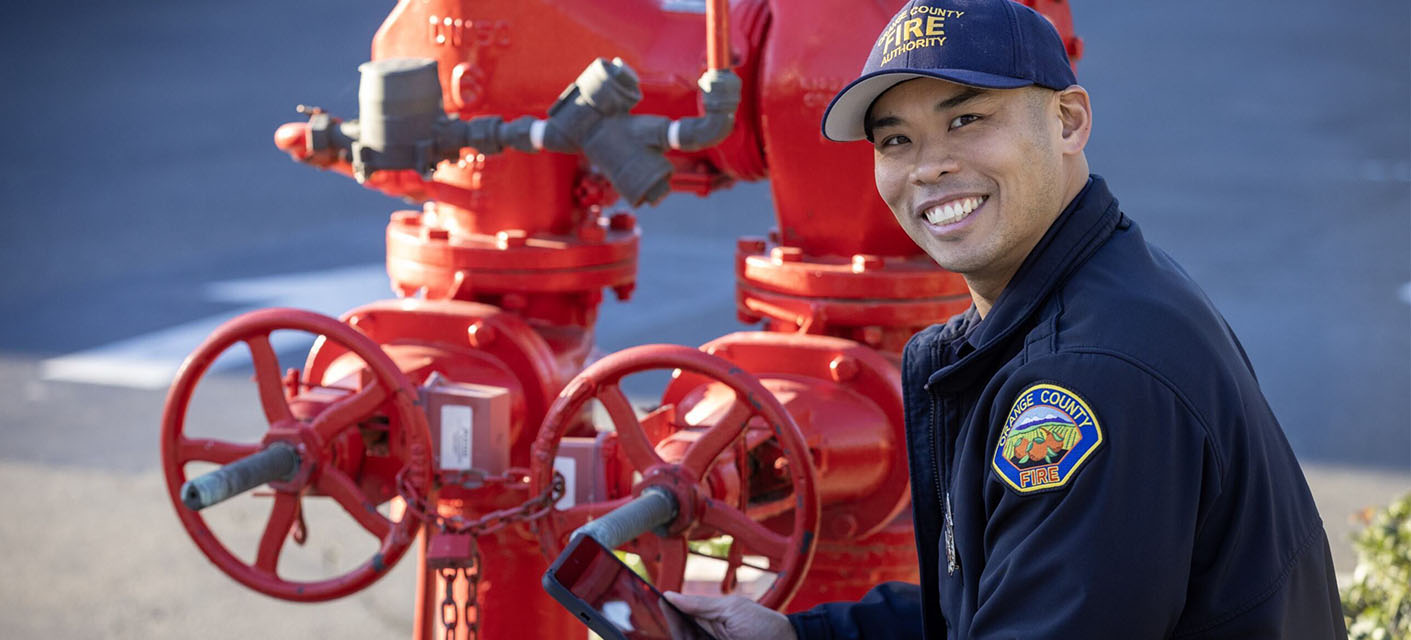 A smiling fire inspector kneels in front of a red fire hydrant