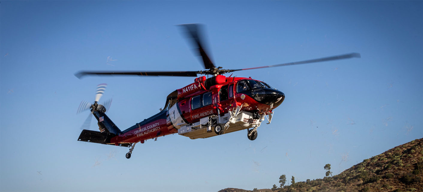 A fire rescue helicopter from OCFA  in flight above a hilly landscape with clear blue sky in the background